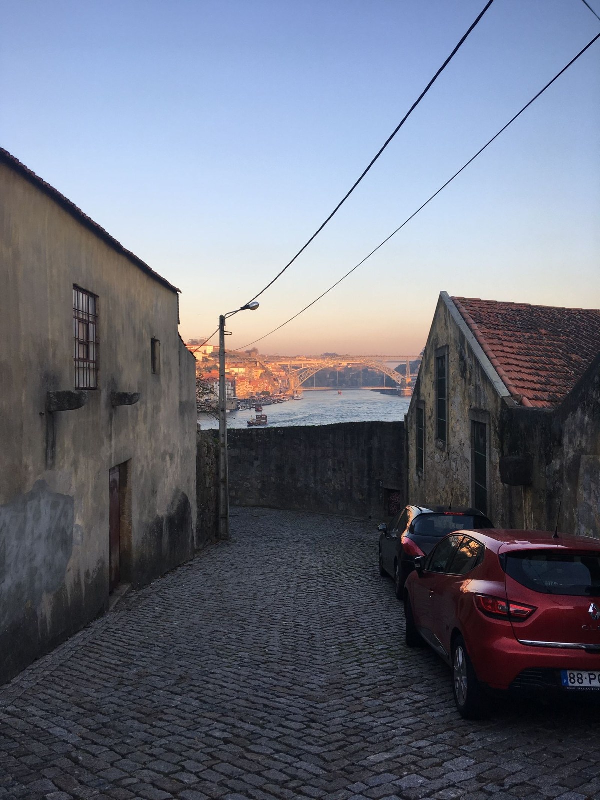 Abfallende gepflasterte Straße mit Brückenblick in Porto