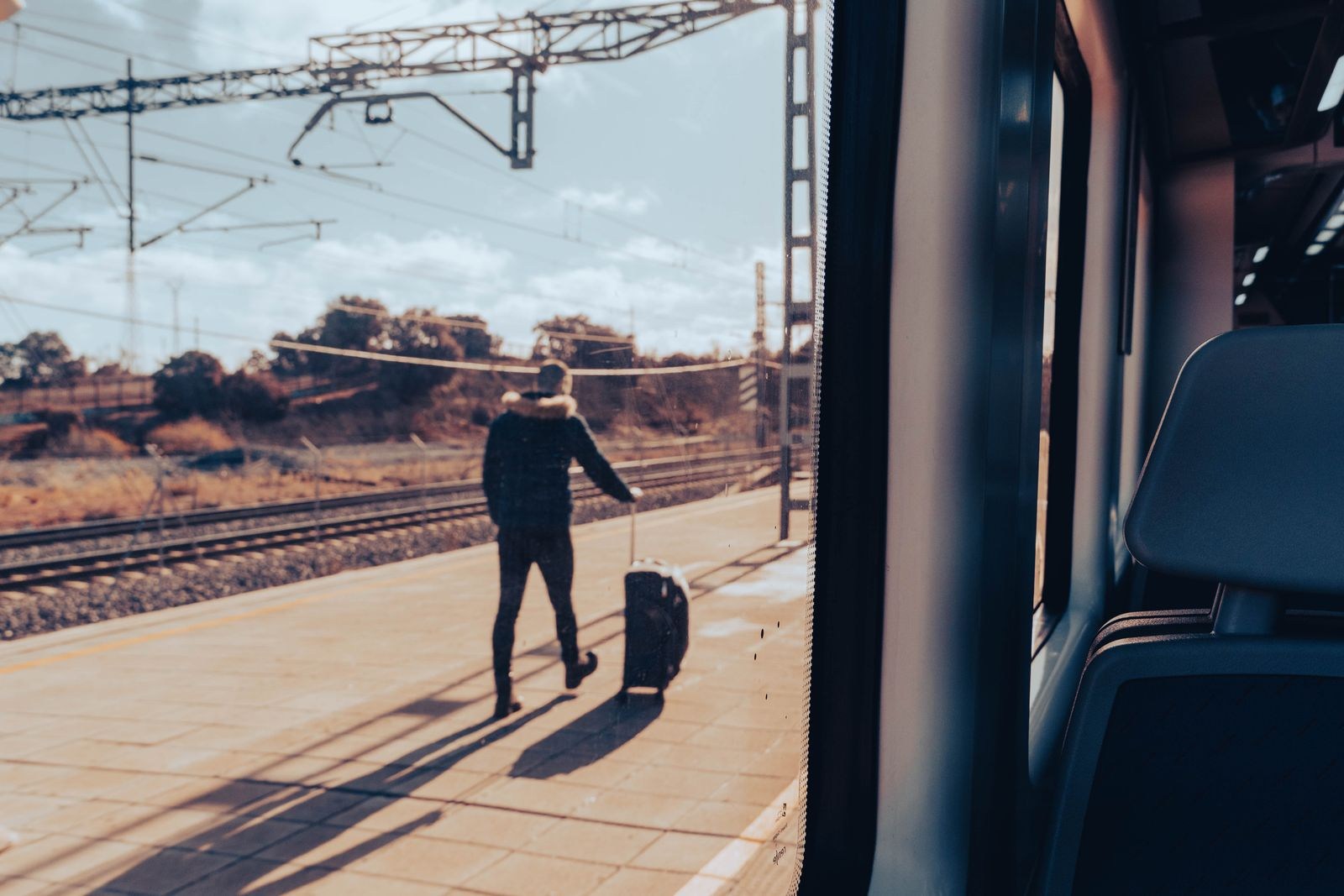 Reisender mit Rollkoffer auf einem Bahnsteig, vom Zug aus gesehen